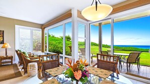 A spacious room with a large glass table, wicker chairs, and a view of a lush green landscape and ocean. - Kapalua Bay | Ocean View 2 BR, Sleeps 8 | Car Incl. w/ 6+ Nights | KBV ML-1996 by KBM (Lahaina)