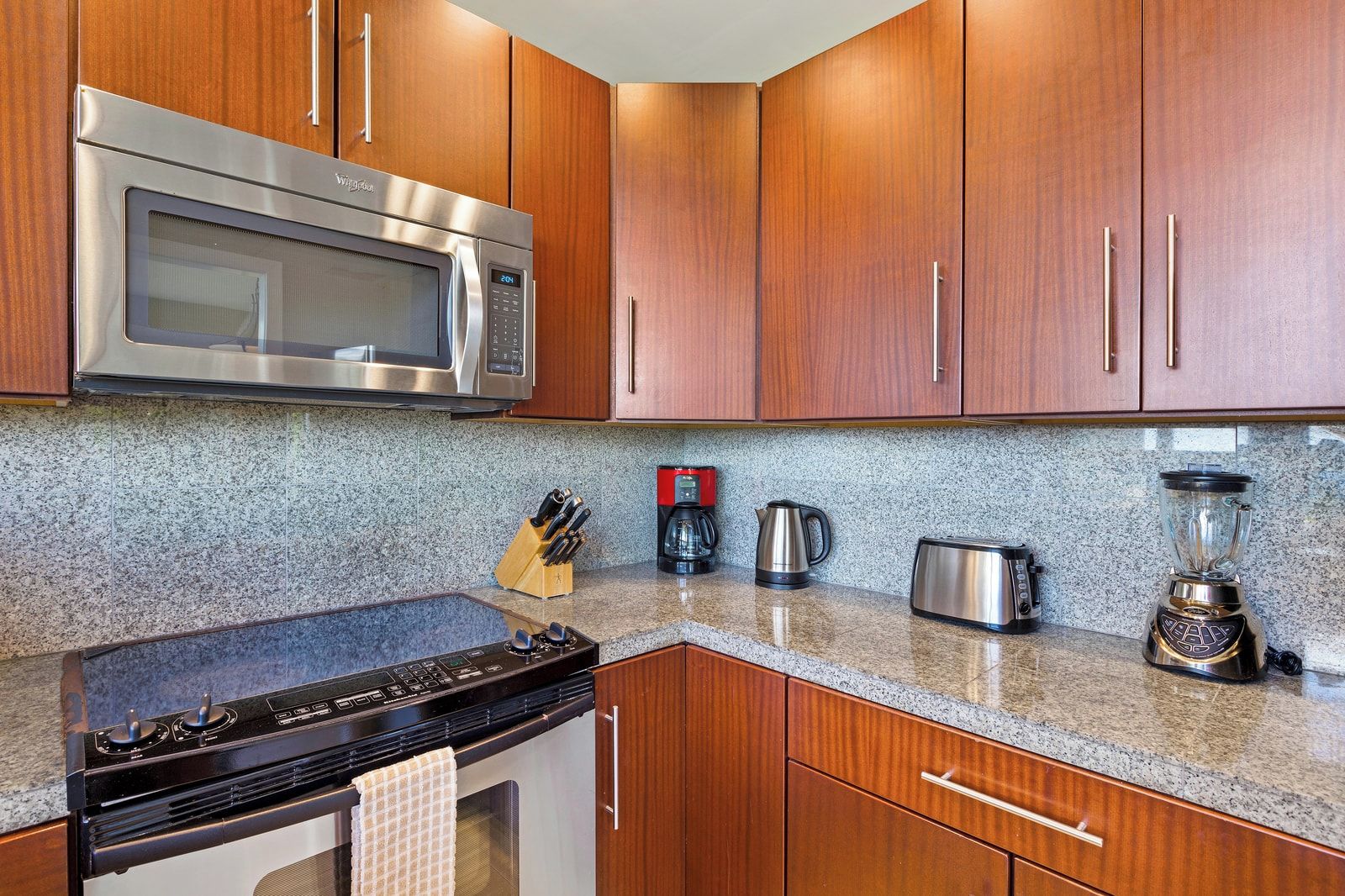 A kitchen with wooden cabinets, a stainless steel microwave, a gas stove, a coffee maker, a toaster, and a blender.
