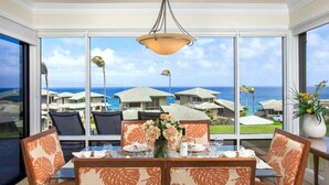 A dining area with a table set for four, large windows offering a view of a coastal area with houses and palm trees. - Kapalua Bay | Ocean View 3 BR, Sleeps 10 | Car Incl. w/ 6+ Nights | KBV ML-2014 by KBM (Lahaina)