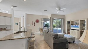 Eine moderne Küche mit Kochinsel, Essbereich mit Sofa und Sesseln, Fernseher und Deckenventilator.