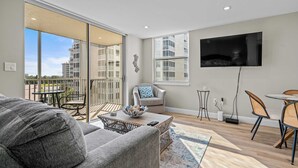 Una sala de estar moderna con un sofá, una mesa de centro, un televisor y un balcón con vistas a edificios.