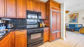 A kitchen with wooden cabinets, a black stove, and a refrigerator. - Kapalua Bay | Ocean View 5 BR, Sleeps 16 | Car Incl. w/ 6+ Nights | KBV ML-2026 by KBM (Lahaina)