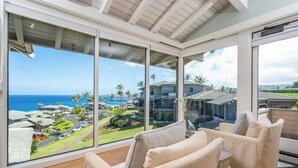 A room with large windows, a wooden ceiling, and a view of a coastal area with buildings and palm trees. - Kapalua Bay | Ocean View 5 BR, Sleeps 16 | Car Incl. w/ 6+ Nights | KBV ML-2026 by KBM (Lahaina)