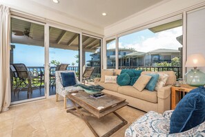 Ein Wohnzimmer mit einer Couch, Sesseln, einem Couchtisch und Blick auf das Meer durch große Fenster.