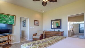 A bedroom with a bed, a TV, a dresser, a chair, and a bathroom visible through an open door. - Kapalua Bay | Ocean View 5 BR, Sleeps 16 | Car Incl. w/ 6+ Nights | KBV ML-2026 by KBM (Lahaina)