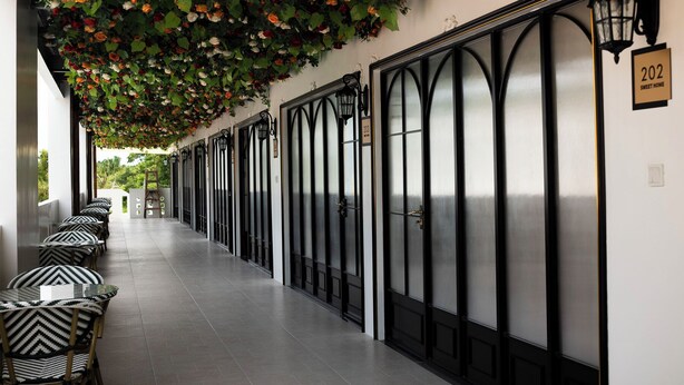 A corridor with black-framed doors, numbered 203 and 202, and a row of black and white patterned chairs on the left. - Madeline Paradise Resort (Panglao)