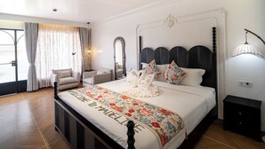 A spacious bedroom with a large bed, a sitting area with chairs, a mirror, and a decorative wall lamp. - Madeline Paradise Resort (Panglao)