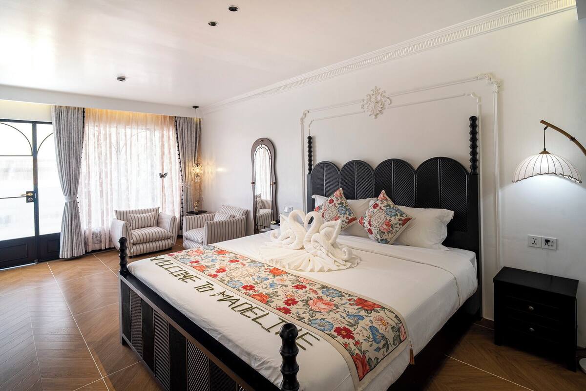Une chambre spacieuse avec un grand lit, un coin salon avec des fauteuils, un miroir et une applique murale décorative.