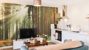 En moderne stue med stort TV, sofa, sofabord og et køkkenområde med vask og komfur.
