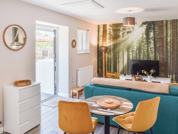 A modern living room with a sofa, two chairs, a coffee table, a TV, and a large forest-themed wall mural.
