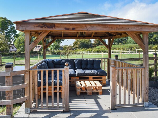 Un kiosque en bois avec un banc et une table, entouré d’une clôture.