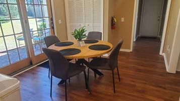 A dining area with a round table, four chairs, and a potted plant.
