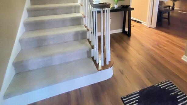 Una escalera con barandilla de madera y balaustres blancos, que conduce a una plataforma con una lámpara y una pequeña mesa.