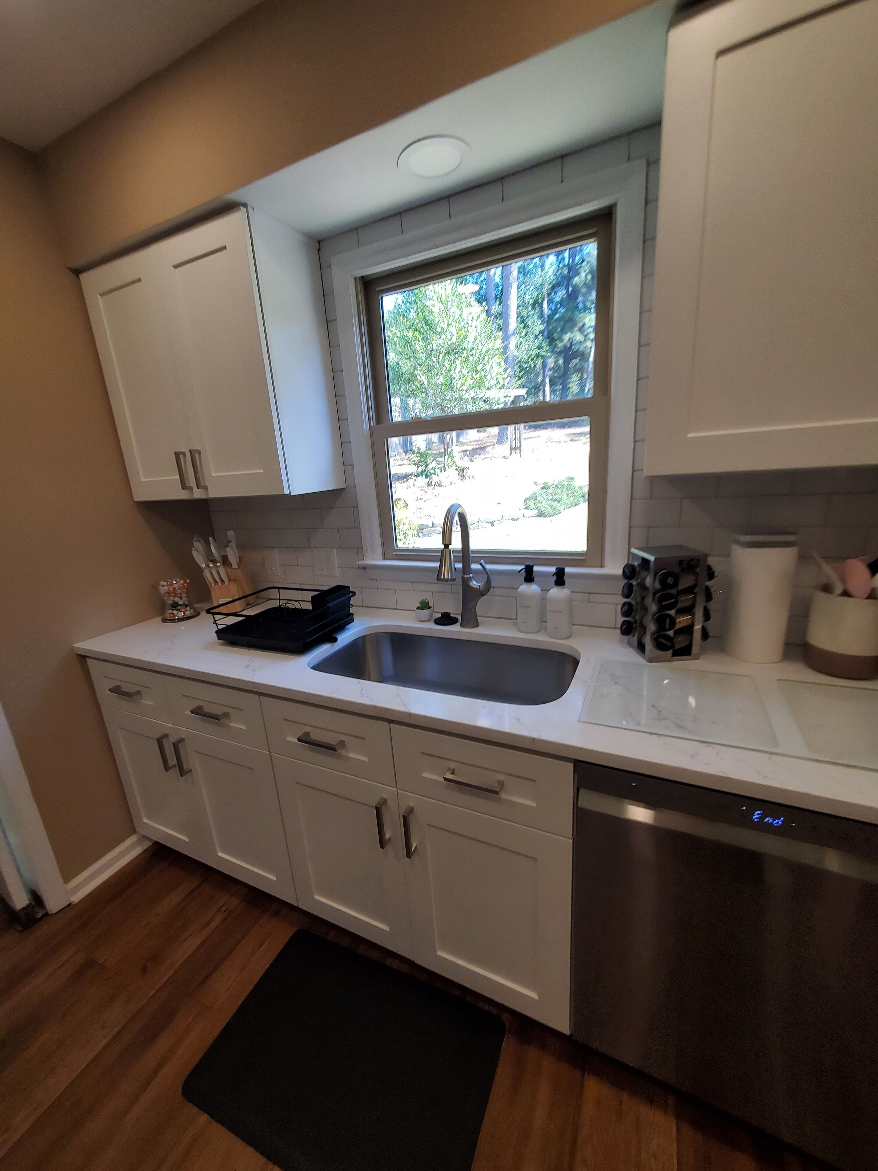 A kitchen with white cabinets, a stainless steel sink, and a window with a view of greenery outside.