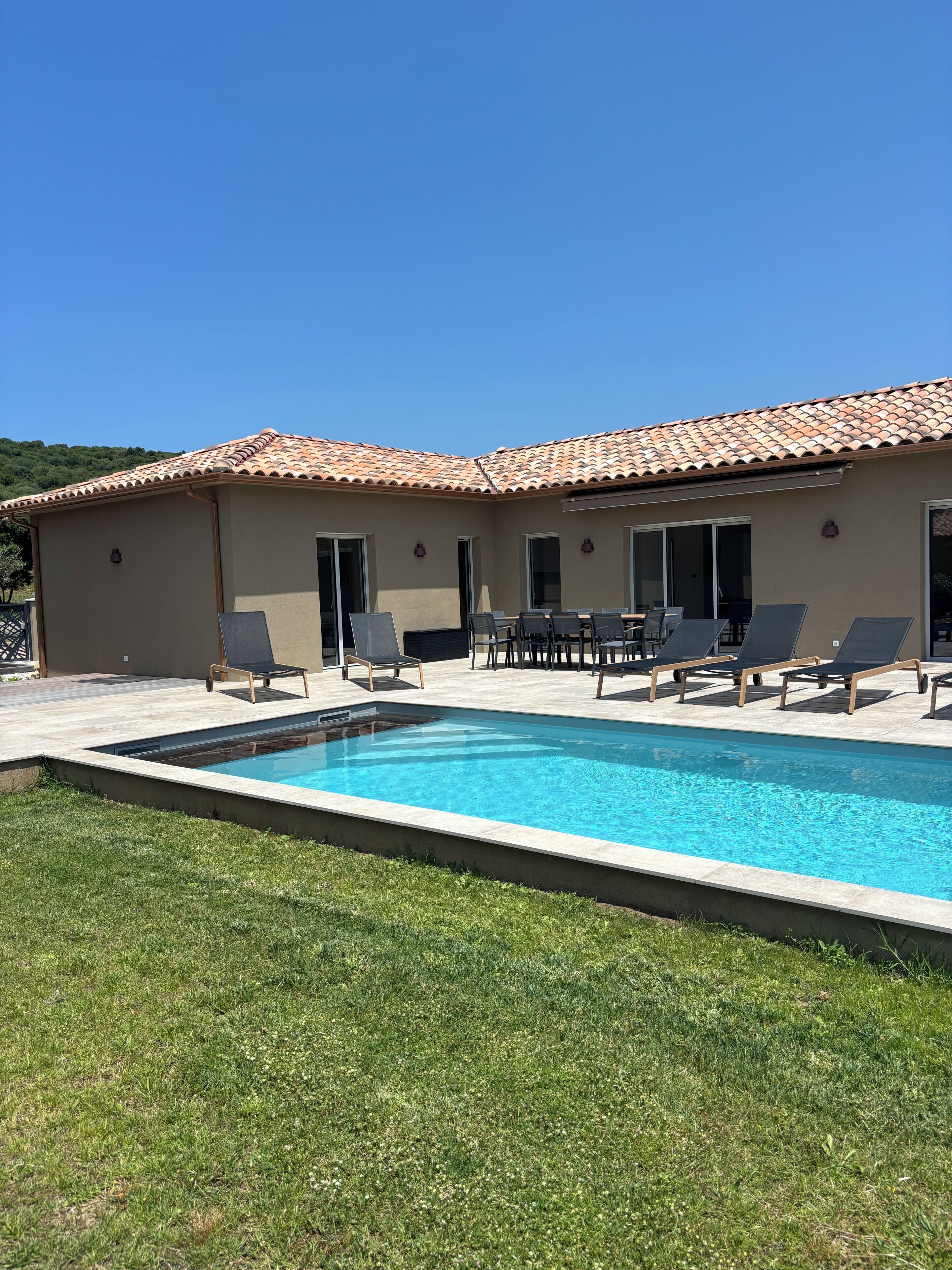 A swimming pool with lounge chairs, a patio area, and a building with a tiled roof.