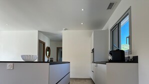 Una cocina moderna con armarios blancos, una isla grande con un bol y un ventanal con vistas.