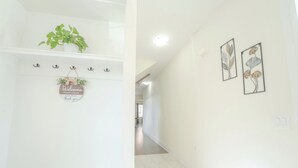 Een gang met een welkomstbord, een plant en twee wanddecoraties met bloemen.