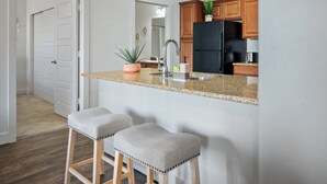 Una cocina con encimera de granito, armarios de madera, un refrigerador negro, un lavamanos y dos taburetes de bar.