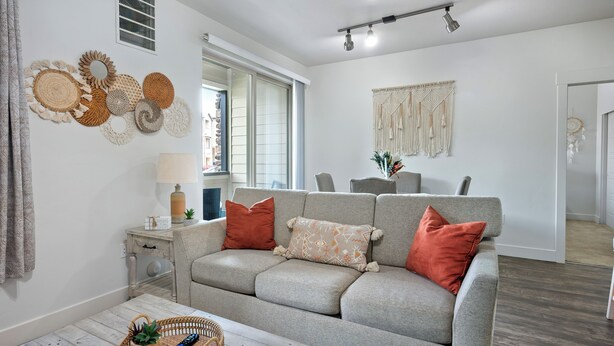 Una sala de estar moderna con un sofá gris, una mesa de centro de madera y una pared decorada con arte tejido.