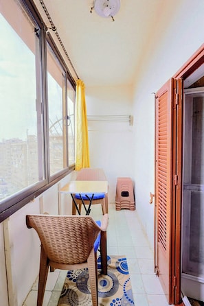 Ein kleiner Balkon mit einem Korbstuhl, einem Tisch und einem gelben Vorhang.