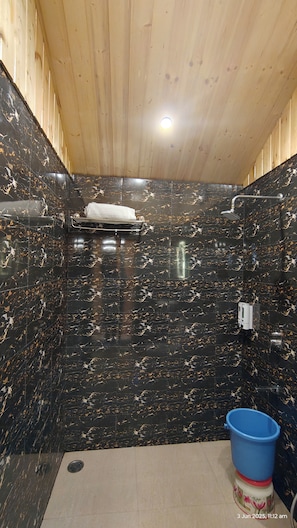 Une salle de bain aux murs recouverts de marbre noir, avec un plafond en bois et un seau bleu posé sur le sol.
