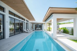 A modern pool area with clear blue water, glass doors, and a covered seating area. - Mouana Mai Khao 3-bedroom Villa M23 (Thalang District)