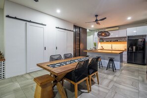 A modern kitchen with a central island, a dining area with a wooden table and chairs, and a ceiling fan. - Villa 121 – Modern 1BR Villa Near Batu Belig Beach (Kabupaten Badung)