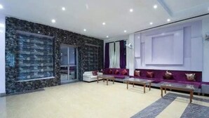 Uma sala de estar espaçosa com piso de mármore, um conjunto de sofás brancos e um conjunto de sofás roxos.