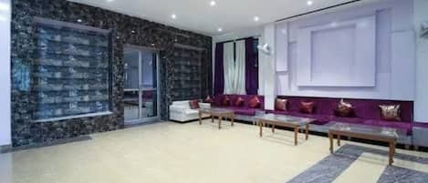 A spacious living room with a marble floor, a white sofa set, and a purple sofa set.