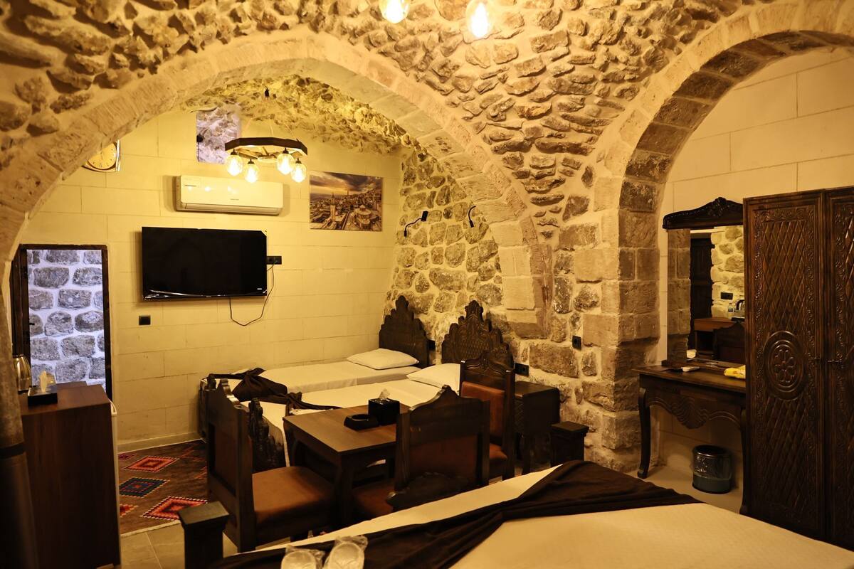 A stone-walled room with a bed, a desk, a chair, a television, and a mirror.