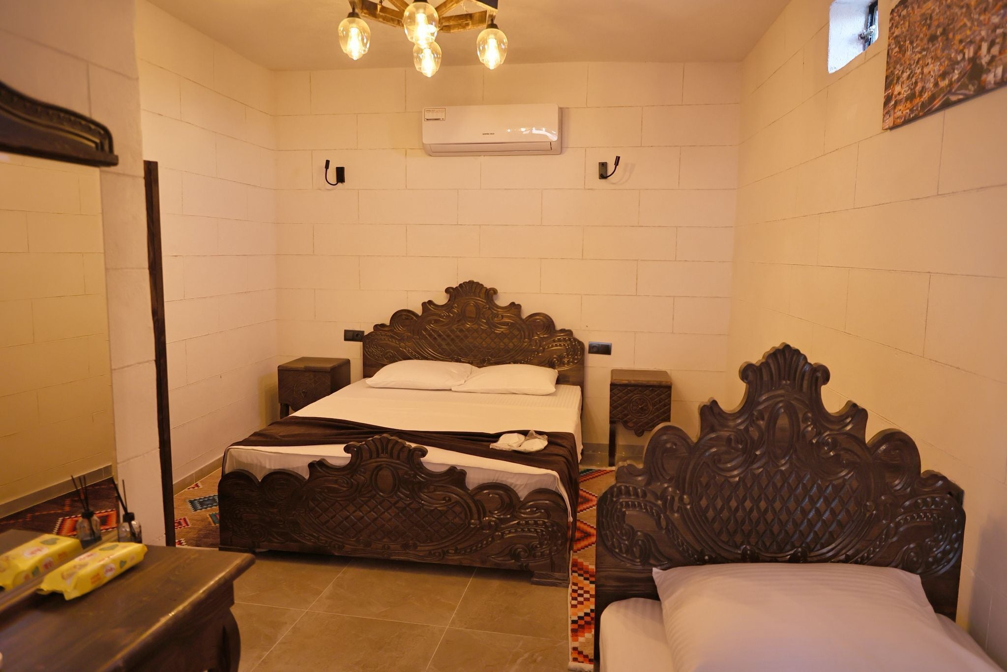 A bedroom with a wooden bed, bedside tables, an air conditioning unit, and a patterned rug.