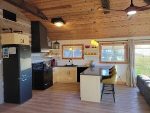 Une cuisine avec des poutres en bois au plafond, un réfrigérateur noir, une cuisinière, un évier et un coin bar avec des tabourets.