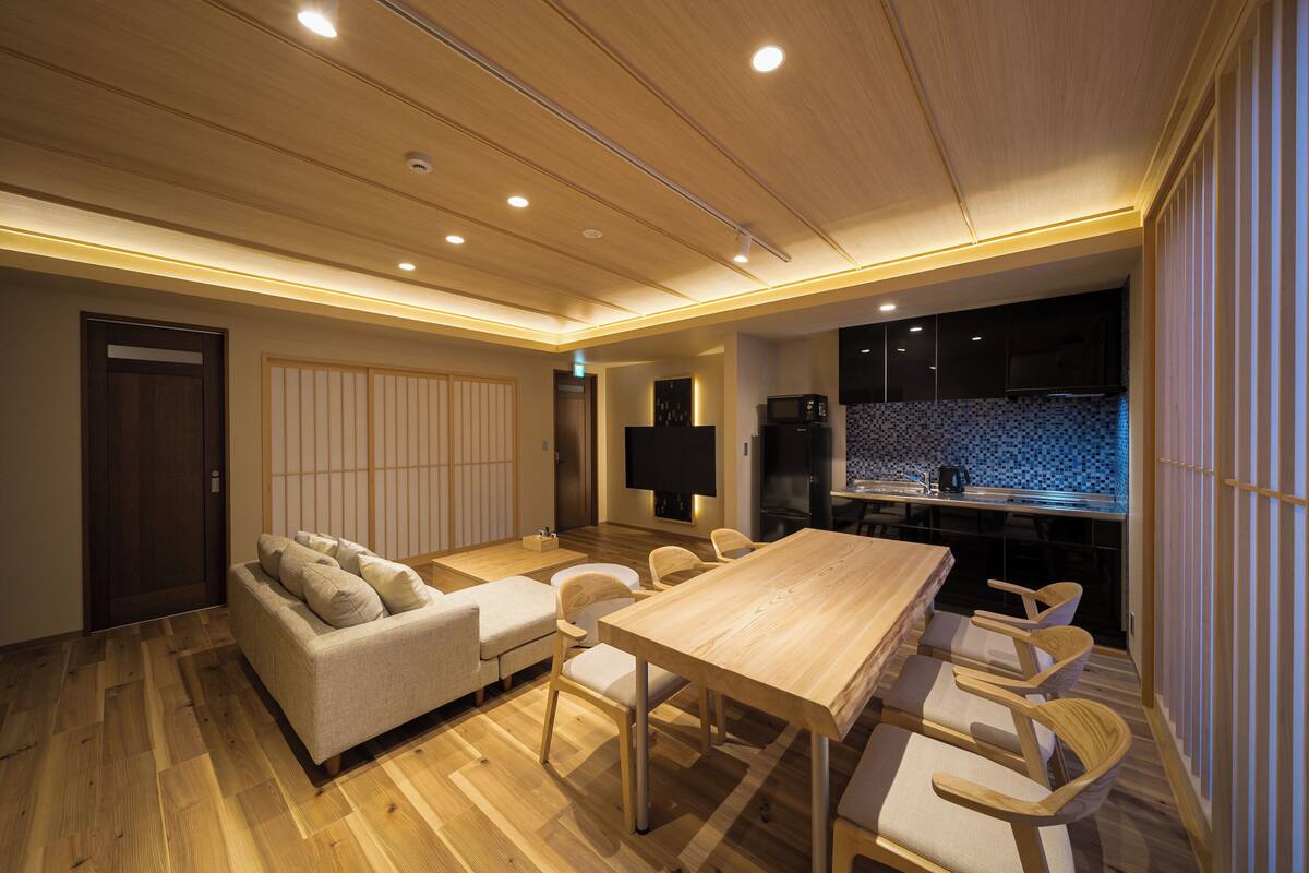 A modern living room with a sofa, chairs, a wooden dining table, and a kitchen area with a microwave and cabinets.