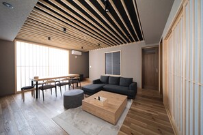 A modern living room with a sectional sofa, a wooden coffee table, and a dining area with a table and chairs. - TAKENOYADO BEPPU (Beppu)