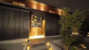 A wooden exterior with a dark entrance, illuminated steps, and a small garden area with plants. - TAKENOYADO BEPPU (Beppu)