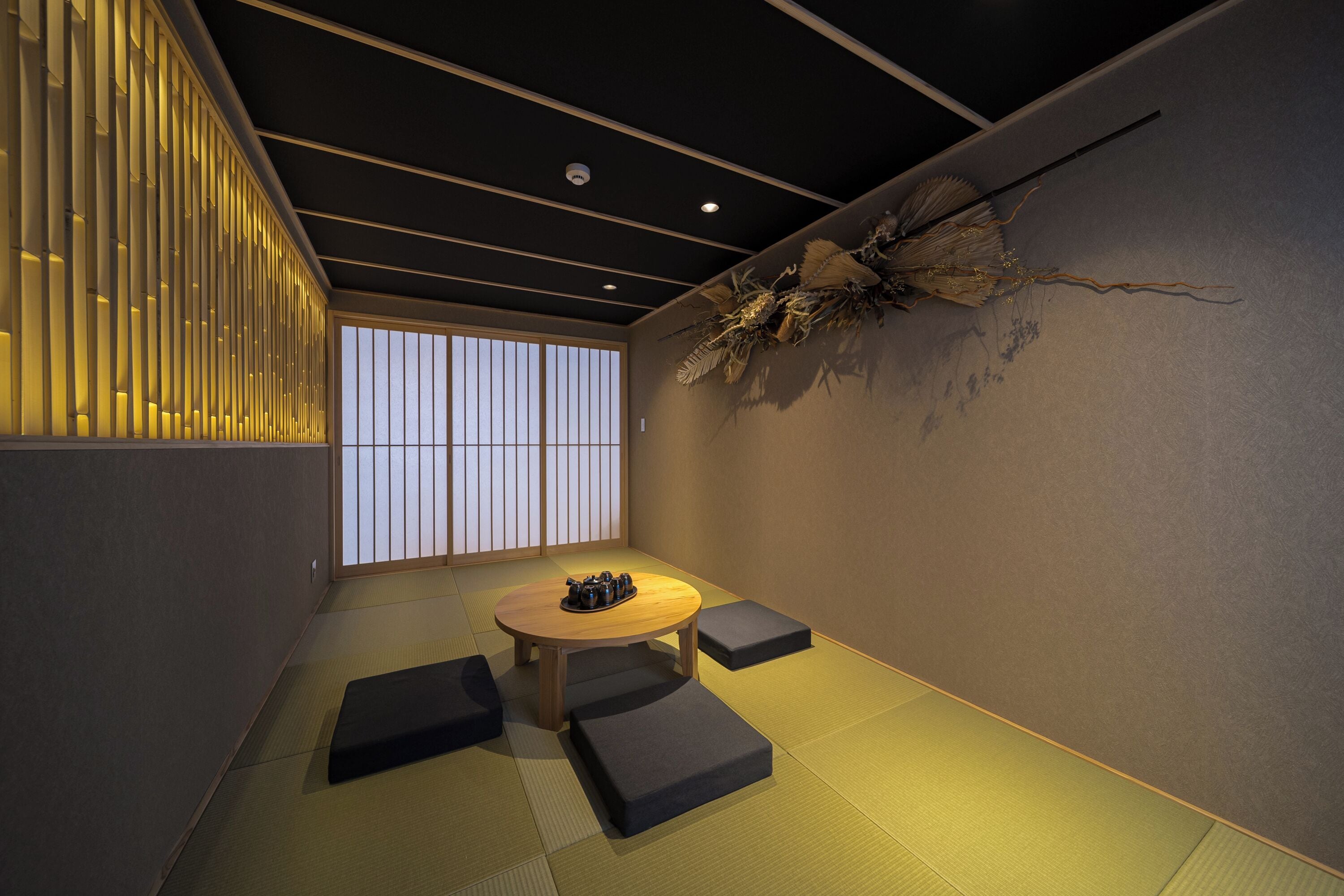 A traditional Japanese room with tatami flooring, a low wooden table, cushions, and a decorative wall piece.