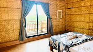 A room with a bed, a window with curtains, and a view of a wooden deck. - Bliss Hampi Eco Resort (Koppal)