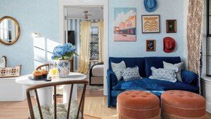 Una sala de estar acogedora con un sofá azul, una mesa de centro con un jarrón de flores y un comedor con una silla y una mesa.
