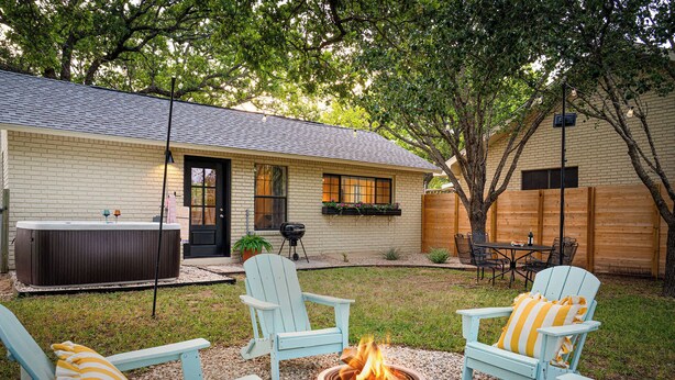 Un patio trasero con una chimenea, dos sillas Adirondack, un jacuzzi y una terraza de madera.
