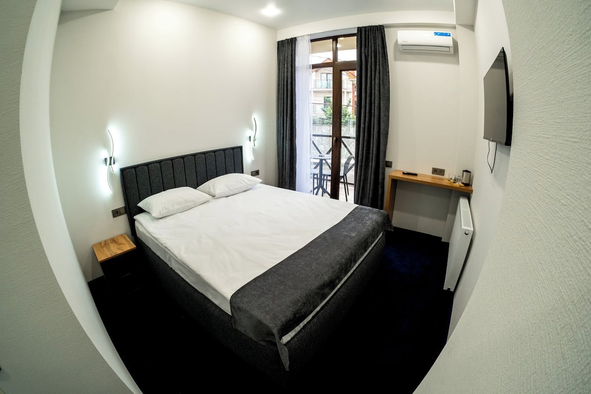 Una camera d'albergo con un letto, un comodino, una televisione e un balcone con tavolo e sedie.