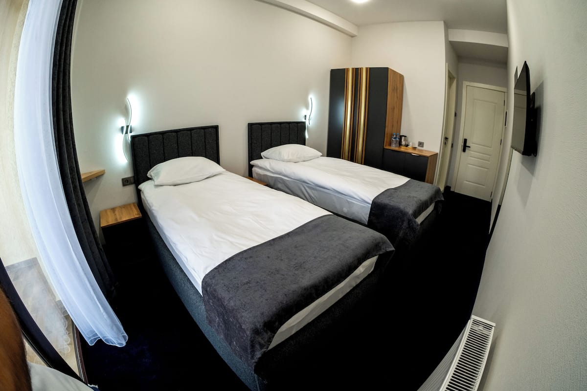 Camera d'albergo con due letti, un armadio, un comodino, uno specchio e una televisione.