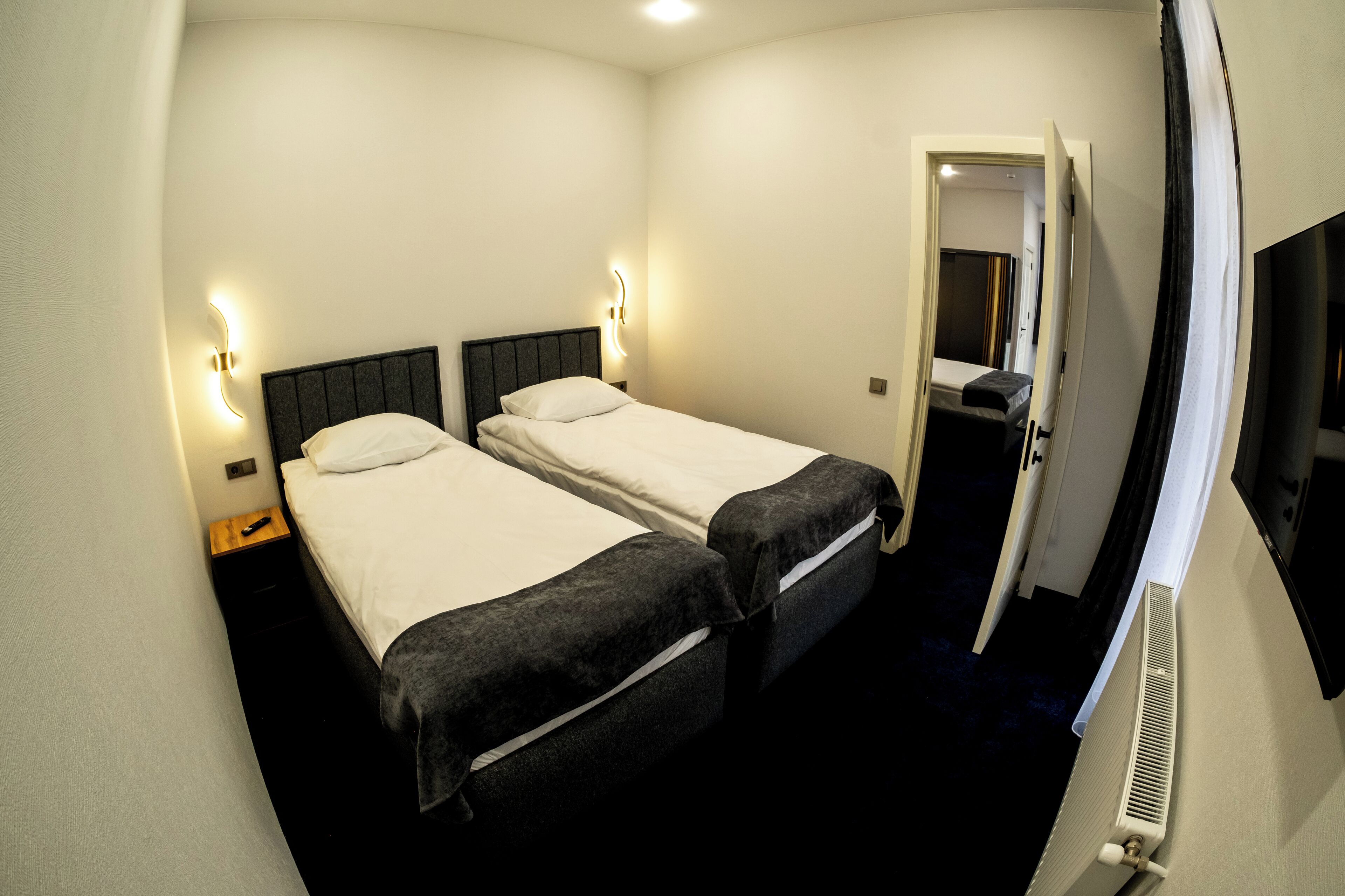 A hotel room with two beds, a radiator, and a door leading to another room.