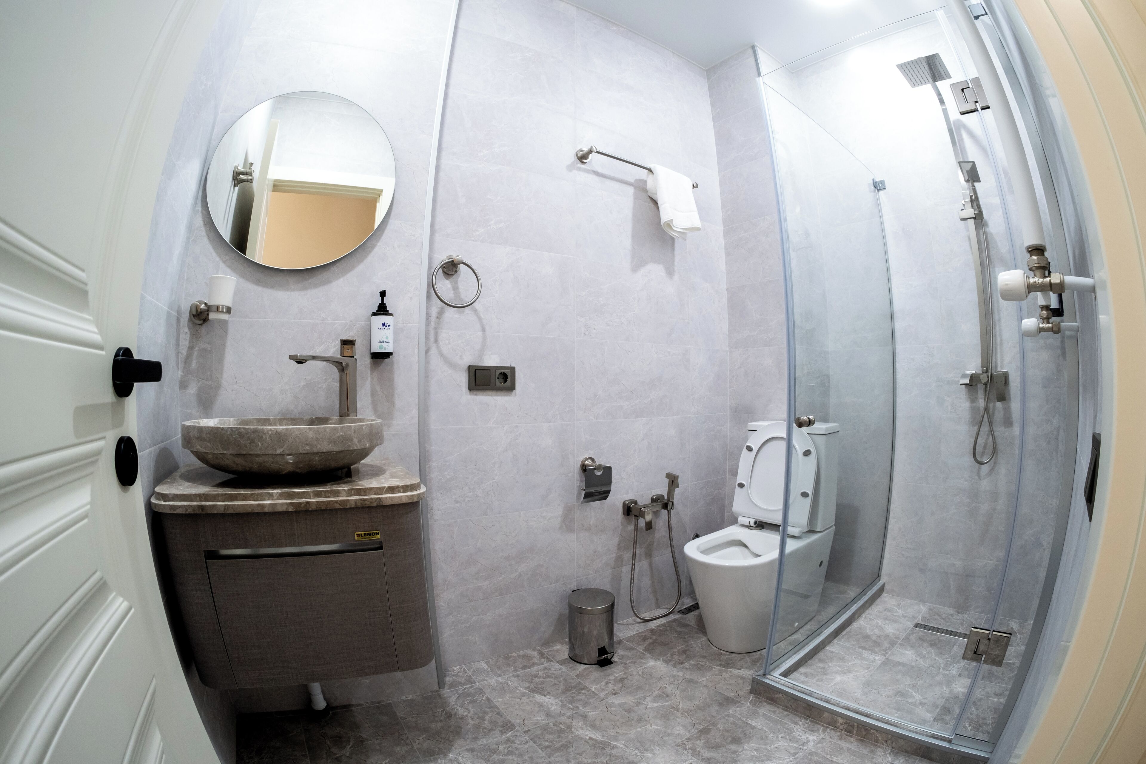 A modern bathroom with a round mirror, a sink, a toilet, and a glass-enclosed shower.