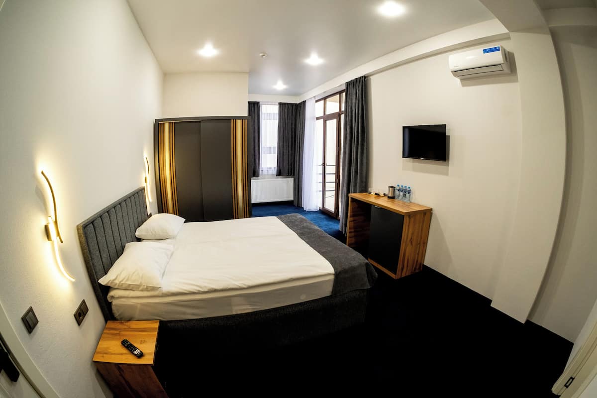 Una camera d'albergo con un letto, un comodino, una televisione e un condizionatore d'aria.