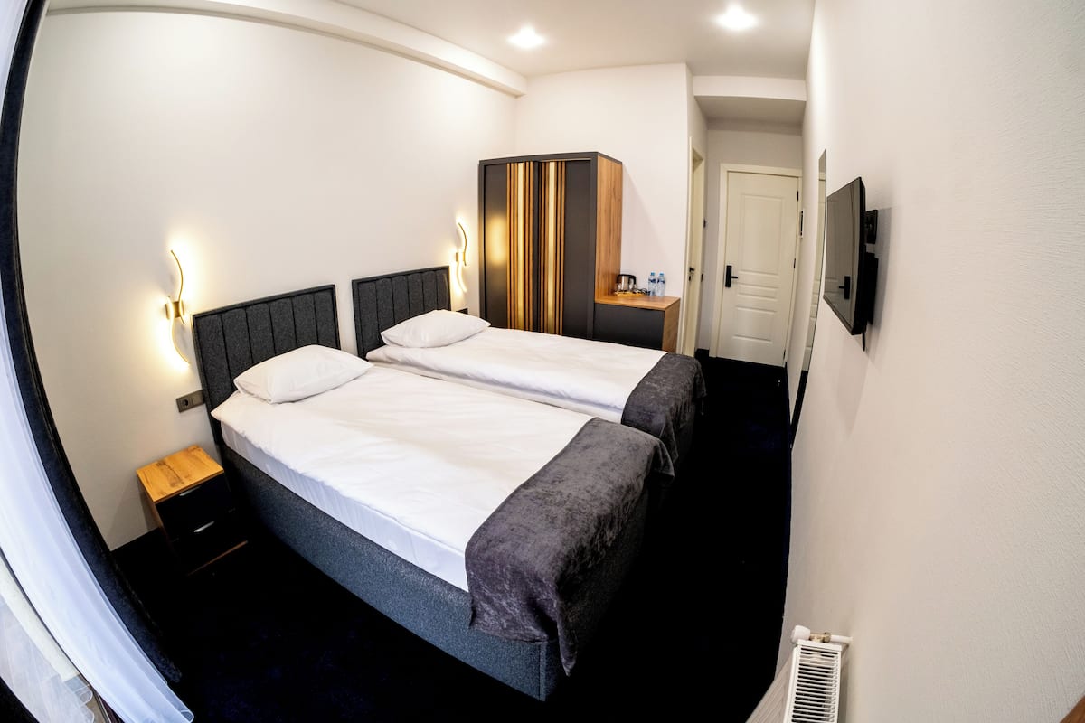 Una camera d'albergo con due letti, un armadio, un comodino, uno specchio e una televisione.