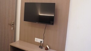 Μια τηλεόραση τοποθετημένη στον τοίχο, πάνω σε ένα ξύλινο πάνελ, με ένα ράφι από κάτω.