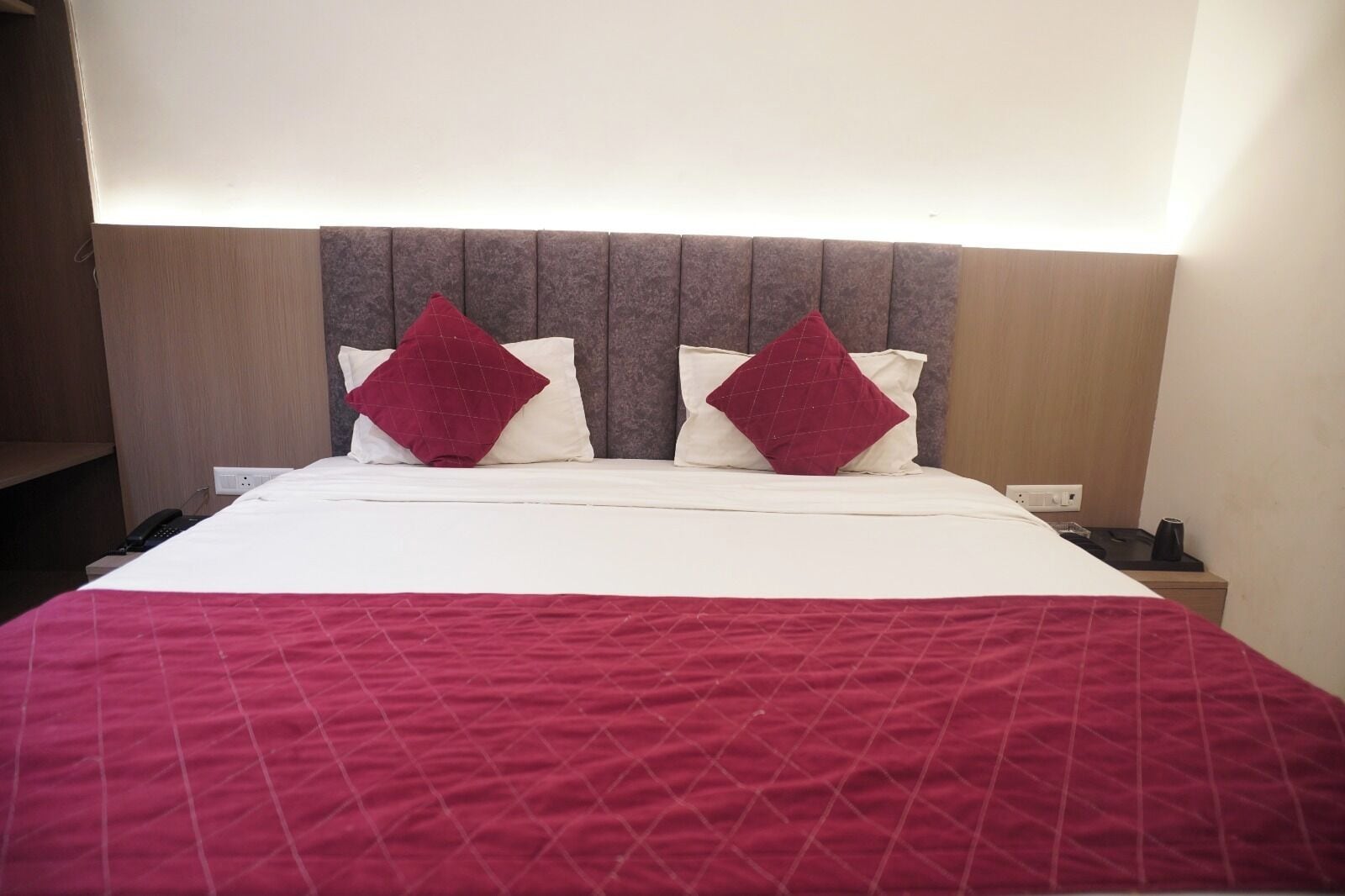 A hotel room with a bed, two pillows, a bedside table, and a nightstand.