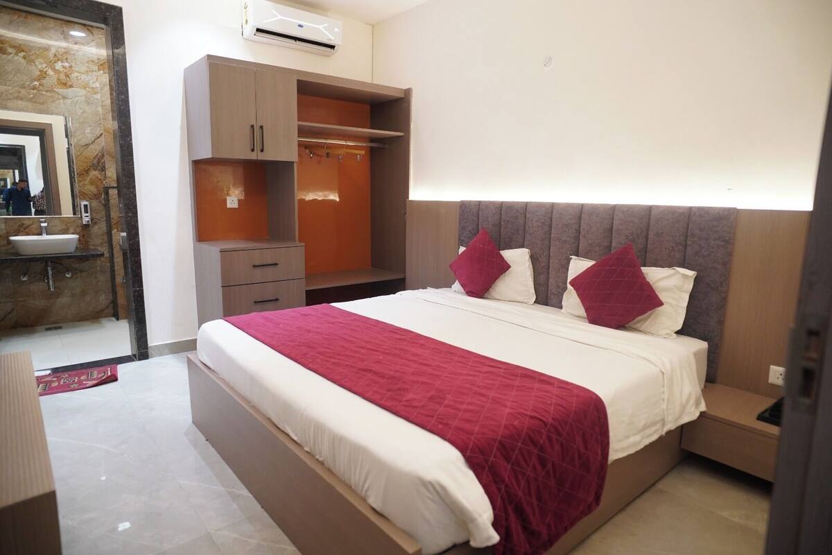 A hotel room with a bed, a wardrobe, a bedside table, and a bathroom visible through an open door.