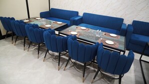 Ένας χώρος τραπεζαρίας με ένα τραπέζι με γυάλινη επιφάνεια, μπλε ταπετσαρισμένες καρέκλες και έναν μαρμάρινο τοίχο στο βάθος.