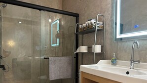 A modern bathroom with a glass shower enclosure, a white toilet, a sink with a mirror, and shelves with towels and toiletries. - Marvelous 3-bedroom house with AC in Inglewood (Inglewood)